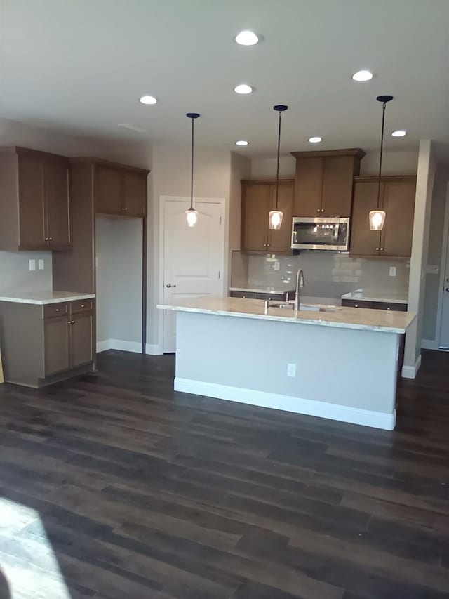 986 S Koleen Ave, Kerman, CA 93630 - kitchen with stainless steel microwave, a sink, dark wood-style flooring, decorative backsplash, and an island with sink