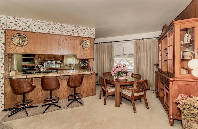 5082 N Maroa Ave, Fresno, CA 93704 - kitchen featuring tile counters, stainless steel appliances, light colored carpet, a kitchen breakfast bar, and brown cabinetry