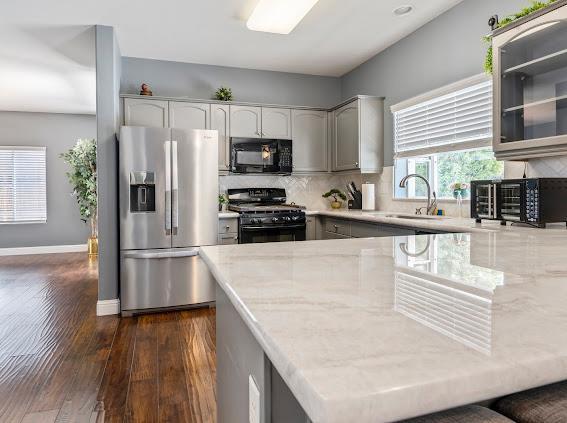 kitchen featuring black appliances, light stone countertops, dark wood-type flooring, tasteful backsplash, and a sink