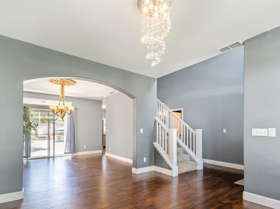 unfurnished room featuring a chandelier, arched walkways, wood finished floors, and baseboards