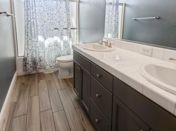 full bathroom featuring toilet, wood finished floors, double vanity, and shower / bathtub combination with curtain
