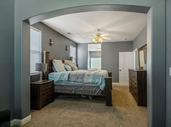 bedroom with light colored carpet, arched walkways, and a ceiling fan