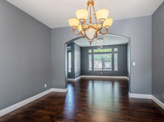 empty room featuring a chandelier, arched walkways, wood finished floors, and baseboards