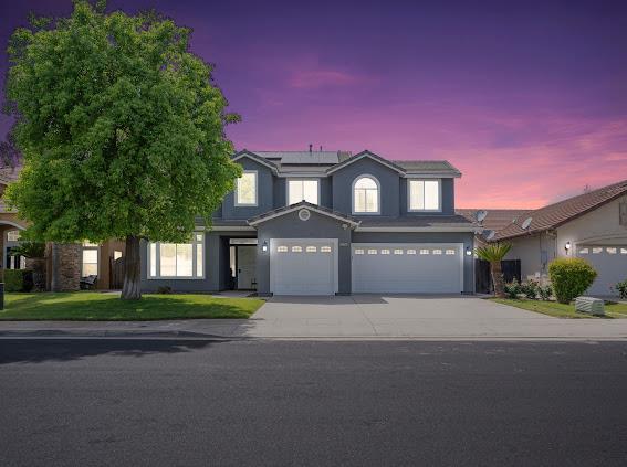 traditional home featuring driveway, an attached garage, stucco siding, roof mounted solar panels, and a front yard