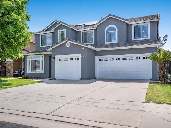 traditional-style house featuring a garage, stucco siding, driveway, and roof mounted solar panels