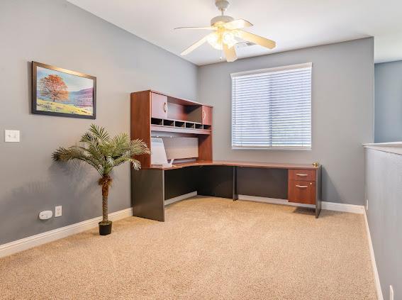 unfurnished office featuring light carpet, ceiling fan, and baseboards