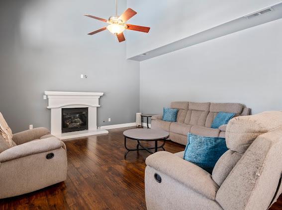 living area with a ceiling fan, wood finished floors, a glass covered fireplace, a high ceiling, and baseboards