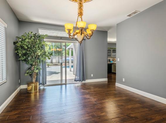 spare room featuring a chandelier, plenty of natural light, wood finished floors, and baseboards
