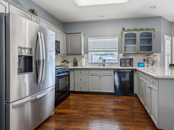 kitchen featuring black appliances, a sink, tasteful backsplash, glass insert cabinets, and recessed lighting
