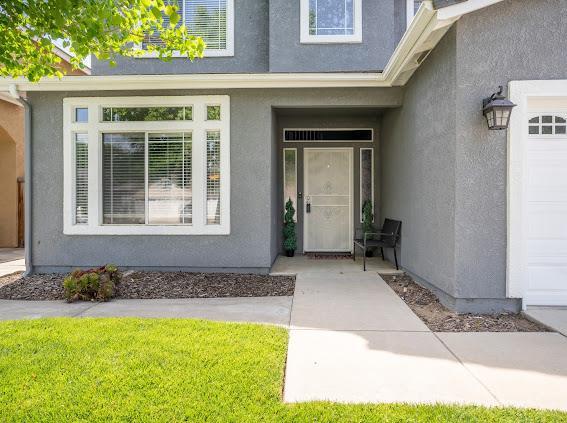 view of exterior entry with stucco siding and a lawn