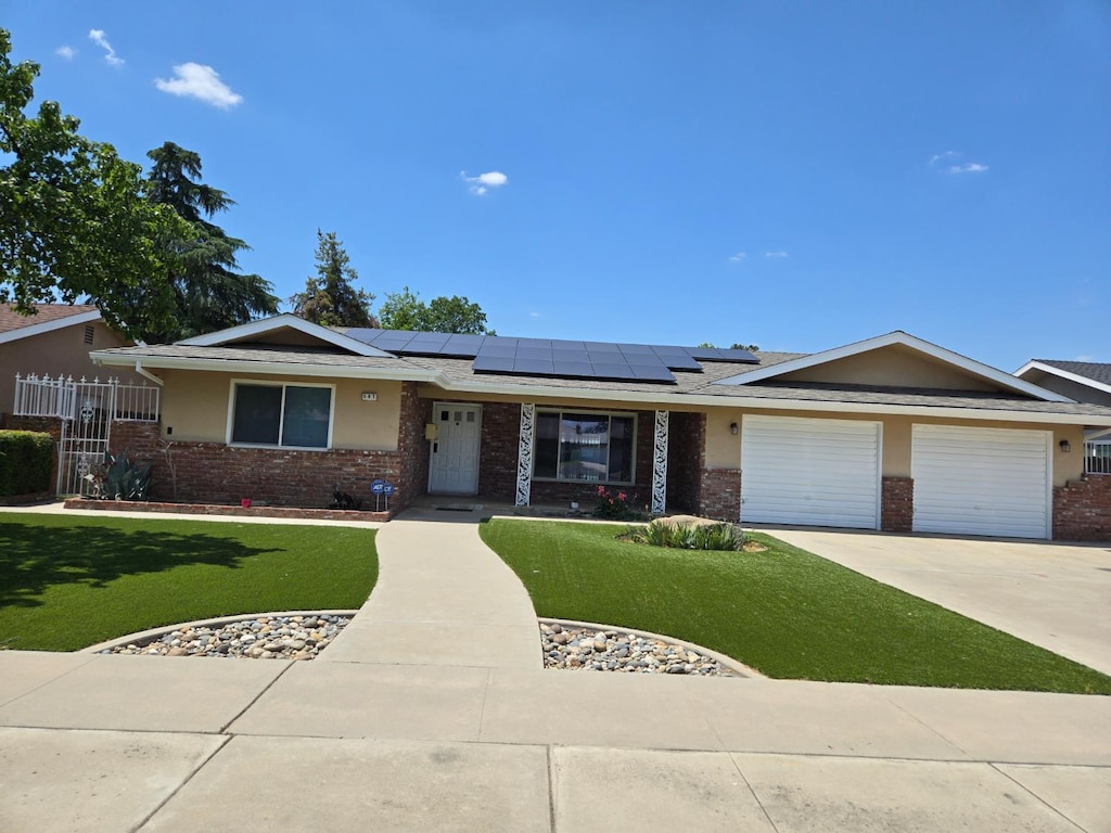 587 N Bates Ave, Dinuba, CA 93618 - ranch-style home with brick siding, roof mounted solar panels, concrete driveway, and an attached garage