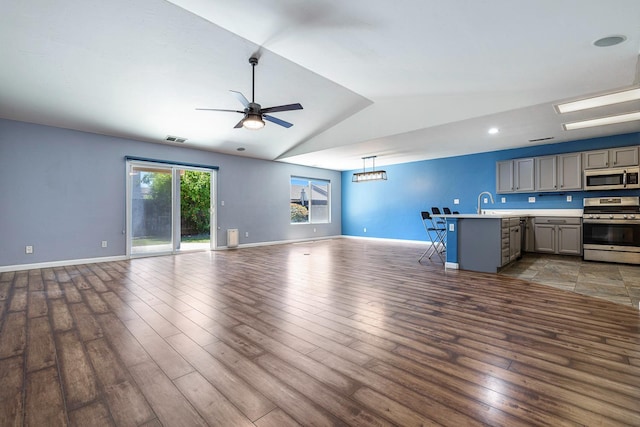 unfurnished living room featuring a ceiling fan, vaulted ceiling, wood finished floors, baseboards, and a sink