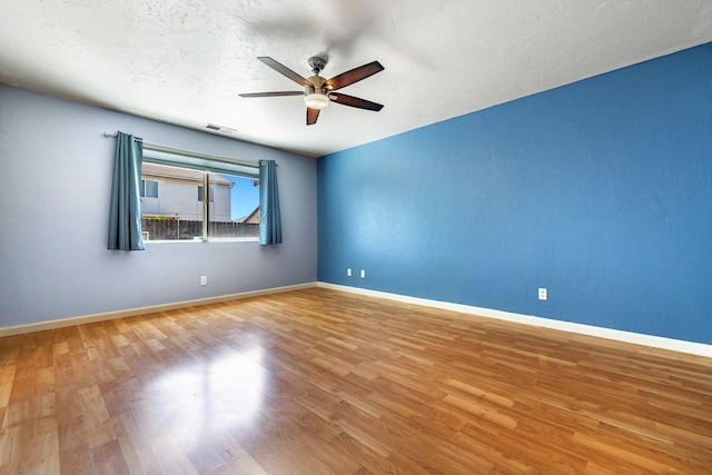 unfurnished room featuring a ceiling fan, wood finished floors, baseboards, and a textured ceiling