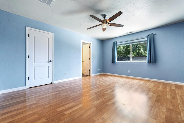 empty room with ceiling fan, light wood finished floors, a textured wall, and baseboards