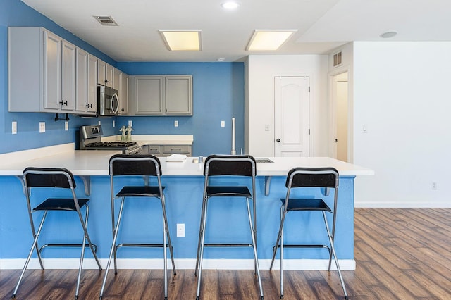 kitchen with appliances with stainless steel finishes, dark wood-style flooring, light countertops, a breakfast bar, and a peninsula