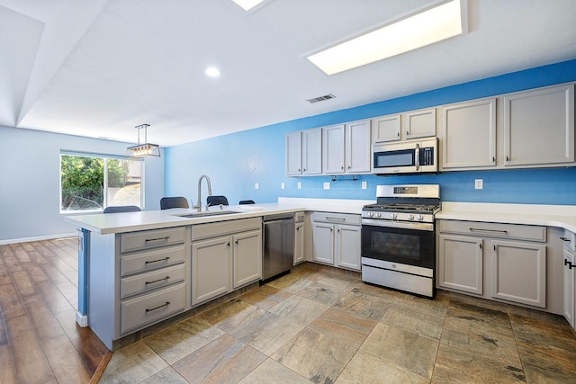 kitchen with stainless steel appliances, a sink, a peninsula, gray cabinetry, and recessed lighting