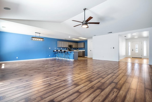 unfurnished living room featuring wood finished floors, a ceiling fan, vaulted ceiling, and baseboards