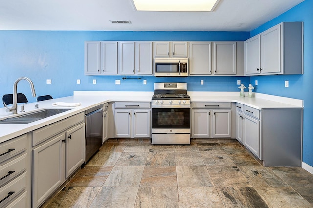kitchen with stainless steel appliances, a sink, stone finish flooring, and gray cabinetry