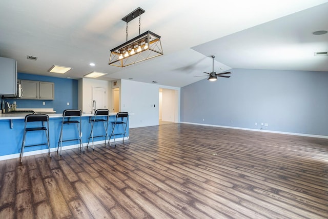 kitchen featuring a kitchen bar, baseboards, dark wood finished floors, a peninsula, and vaulted ceiling