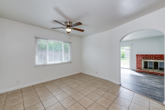 5535 N Millbrook Ave, Fresno, CA 93710 - empty room with arched walkways, light tile patterned flooring, a ceiling fan, a brick fireplace, and baseboards