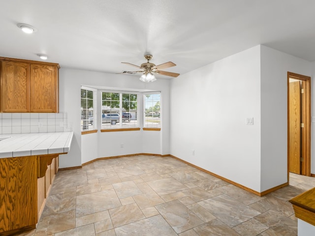 unfurnished dining area with stone finish floors, ceiling fan, and baseboards