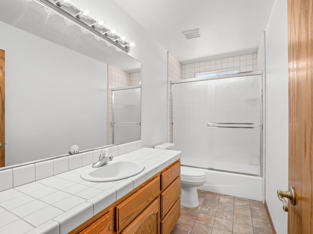 bathroom with toilet, vanity, stone finish flooring, and shower / bath combination with glass door