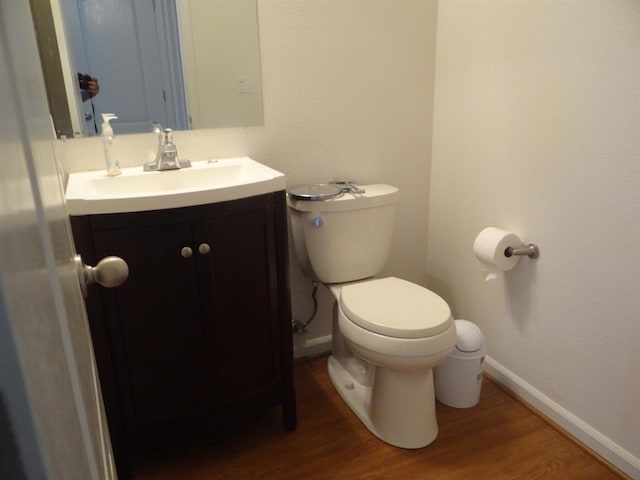 half bath with toilet, vanity, baseboards, and wood finished floors