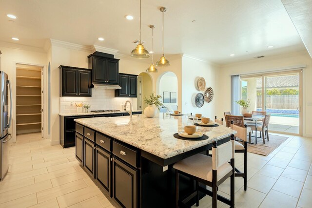 3636 Elberta Cir, Dinuba, CA 93618 - kitchen with a breakfast bar, an island with sink, decorative backsplash, dark cabinets, and light stone counters