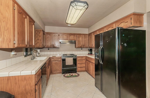 3732 W Garland Ave, Fresno, CA 93722 - kitchen featuring black appliances, a sink, tile counters, under cabinet range hood, and brown cabinetry