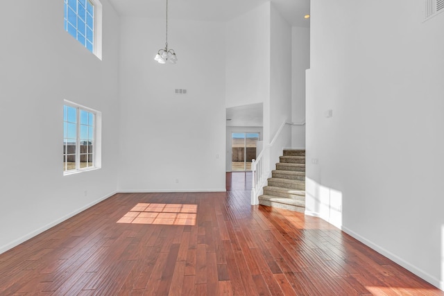 unfurnished living room featuring a high ceiling, stairs, wood finished floors, plenty of natural light, and a chandelier