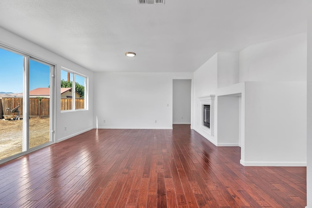 unfurnished living room with dark wood-style floors, baseboards, and a glass covered fireplace