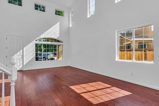 unfurnished living room featuring a high ceiling, wood-type flooring, and baseboards