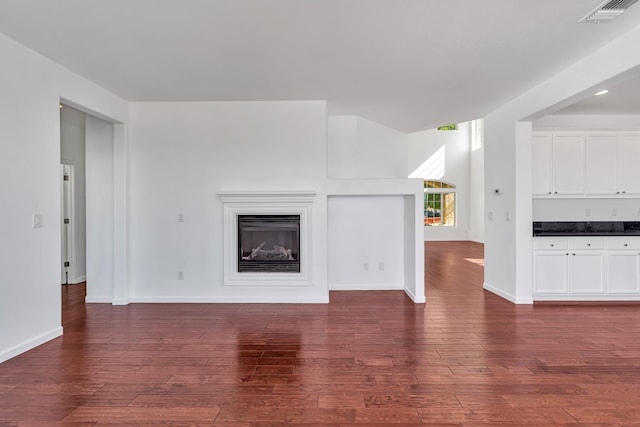 unfurnished living room featuring a glass covered fireplace, dark wood finished floors, and baseboards