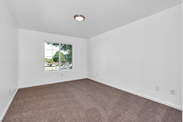 spare room featuring dark colored carpet and baseboards