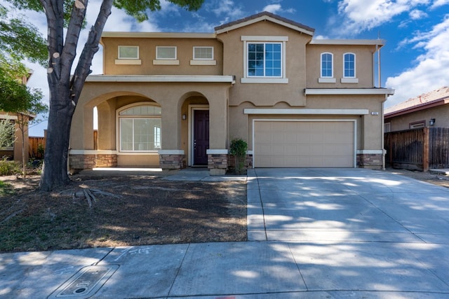 mediterranean / spanish-style home featuring stone siding, stucco siding, fence, a garage, and concrete driveway