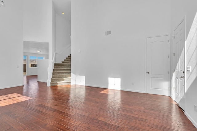 unfurnished living room with a towering ceiling, stairway, wood finished floors, and baseboards
