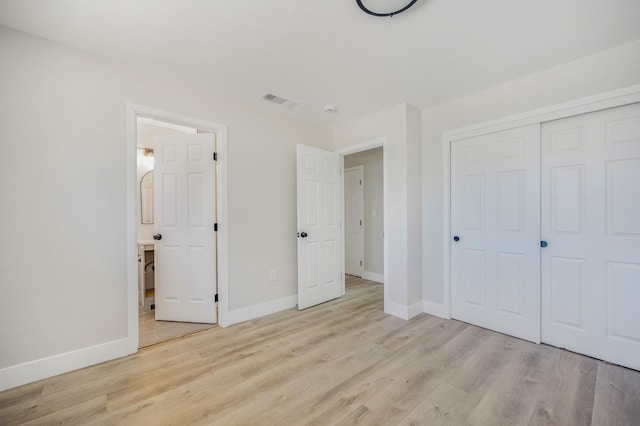 unfurnished bedroom with light wood-style flooring, baseboards, a closet, and ensuite bath