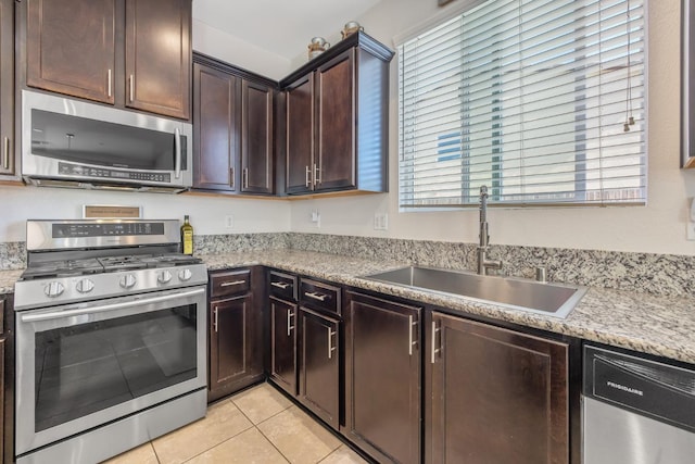 kitchen with stainless steel appliances, a sink, dark brown cabinets, light tile patterned floors, and light countertops