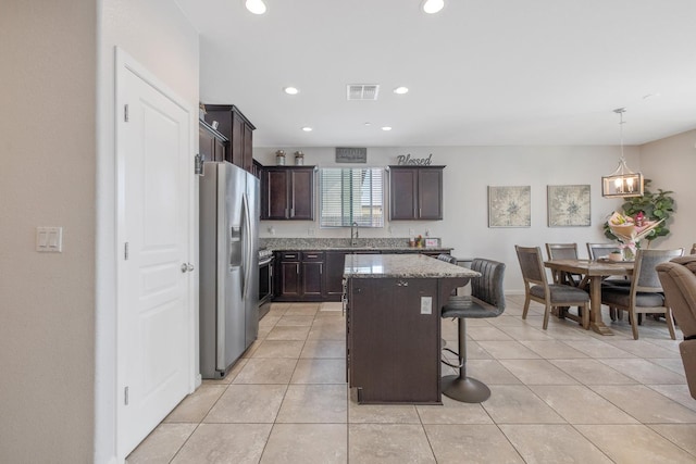 kitchen with appliances with stainless steel finishes, dark brown cabinetry, a kitchen bar, stone counters, and a center island