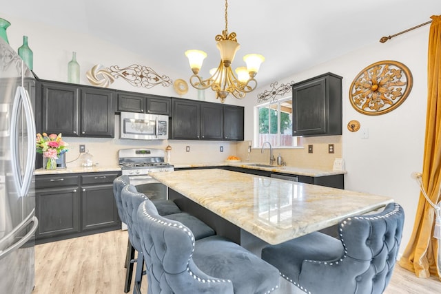 5266 E Harvest Ln, Fresno, CA 93725 - kitchen with appliances with stainless steel finishes, a chandelier, a center island, light stone countertops, and decorative backsplash