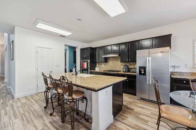 2865 Maine Ave, Clovis, CA 93619 - kitchen featuring appliances with stainless steel finishes, a kitchen bar, a center island with sink, tasteful backsplash, and light wood finished floors