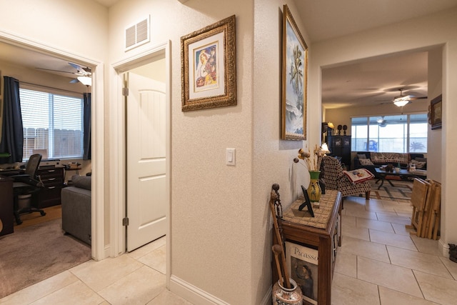 hall featuring a desk, light tile patterned flooring, a textured wall, and baseboards
