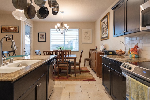 kitchen featuring stainless steel appliances, a sink, a chandelier, pendant lighting, and backsplash