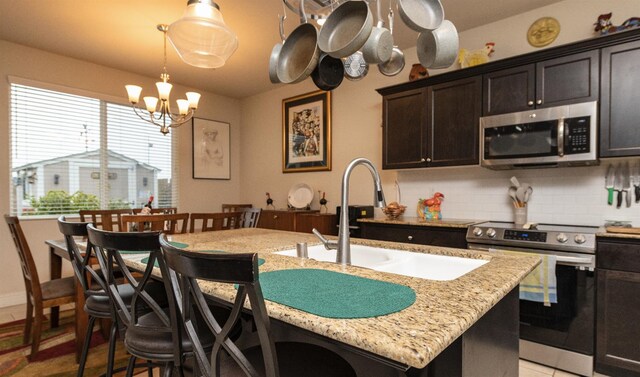kitchen with stainless steel appliances, a chandelier, a sink, decorative backsplash, and light stone countertops