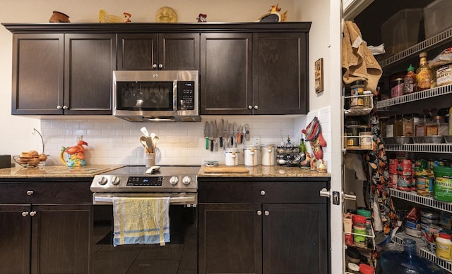 kitchen with appliances with stainless steel finishes, decorative backsplash, dark brown cabinets, and light stone countertops