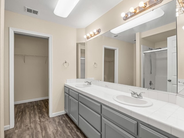 5611 W Carmen Ave, Fresno, CA 93722 - full bathroom featuring a shower stall, wood finished floors, a walk in closet, double vanity, and baseboards