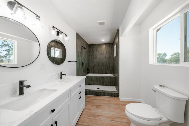 bathroom with toilet, a walk in shower, wood finished floors, double vanity, and baseboards