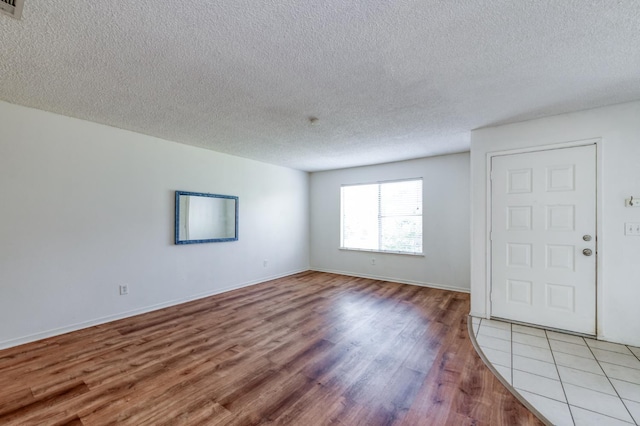 spare room featuring a textured ceiling, light wood finished floors, and baseboards