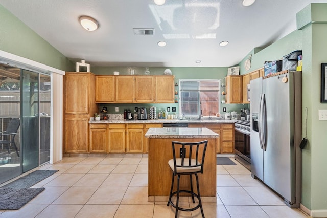 5532 W Indianapolis Ave, Fresno, CA 93722 - kitchen featuring appliances with stainless steel finishes, a center island, a kitchen breakfast bar, and light stone countertops
