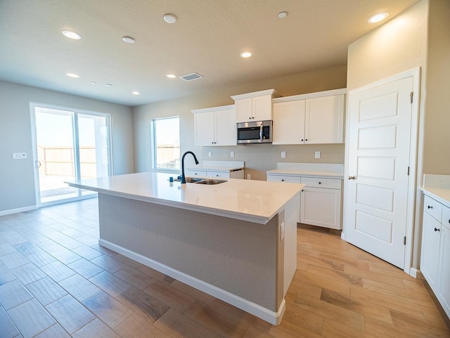 917 Beaver Pond Loop, Madera, CA 93636 - kitchen with stainless steel microwave, a sink, a center island with sink, white cabinetry, and light wood finished floors